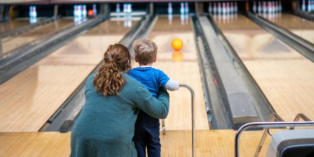 Une femme et un enfant viennent de lancer une boule sur une piste de bowling