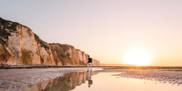 Jeune homme regardant les falaises depuis la plage de Dieppe à marée basse durant le coucher de soleil