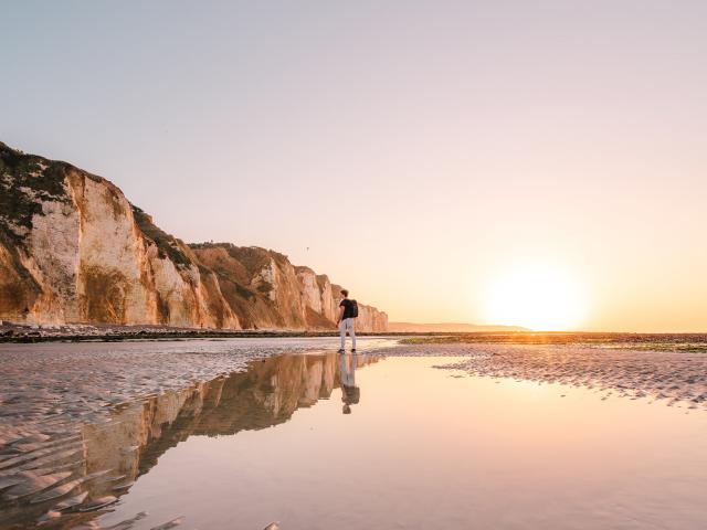 Jeune homme regardant les falaises depuis la plage de Dieppe à marée basse durant le coucher de soleil