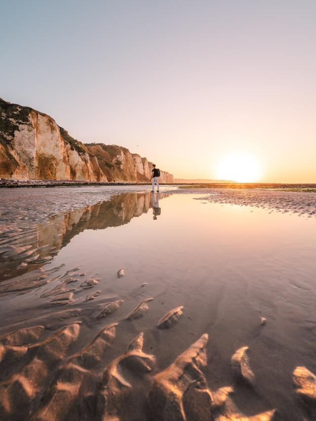 Jeune homme regardant les falaises depuis la plage de Dieppe à marée basse durant le coucher de soleil