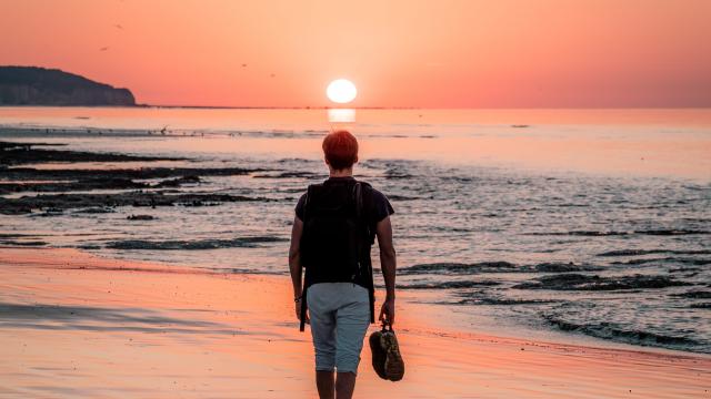 Jeune homme marchant sur la plage de Dieppe à marée basse durant le coucher de soleil