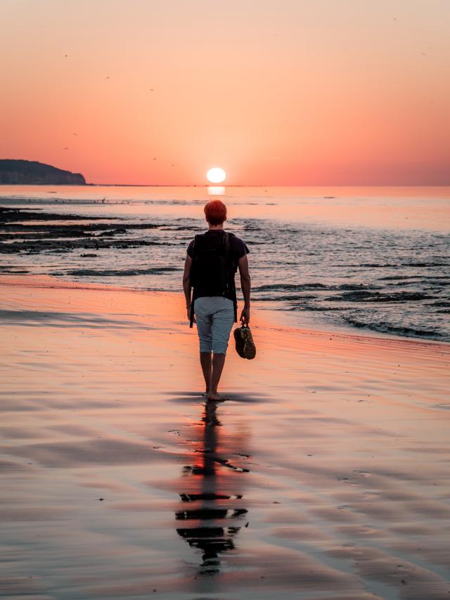 Jeune homme marchant sur la plage de Dieppe à marée basse durant le coucher de soleil