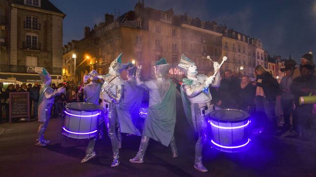 Une fanfare de musiciens au maquillage blanc et aux costumes argentés jouent du tambour sur le quai Henri 4 pendant