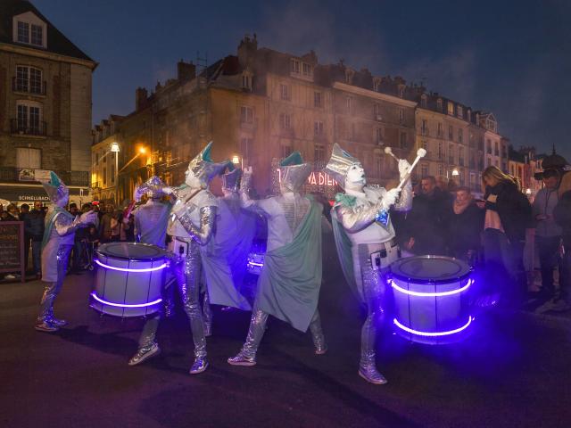 Une fanfare de musiciens au maquillage blanc et aux costumes argentés jouent du tambour sur le quai Henri 4 pendant