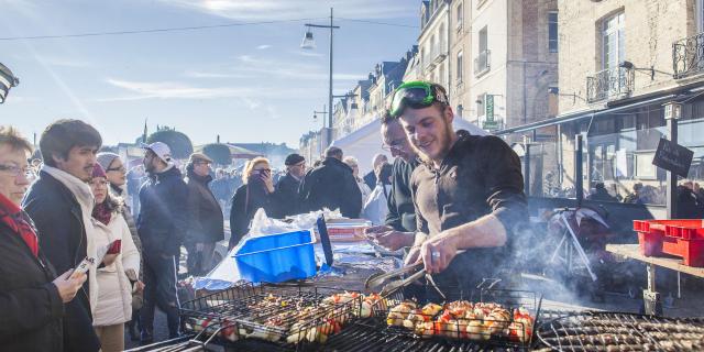 Un jeune homme avec lunettes de plongée sur le front, fait griller des brochettes de coquilles Saint-Jacques devant des passants