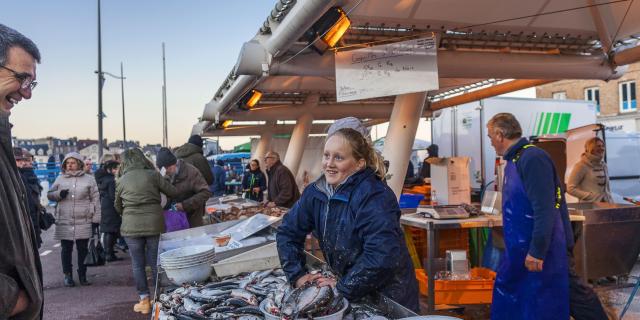 Une jeune femme souriante les mains dans une bassine pleine de harengs sur un étal du marché aux poissons de Dieppe