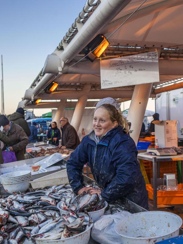 Une jeune femme souriante les mains dans une bassine pleine de harengs sur un étal du marché aux poissons de Dieppe