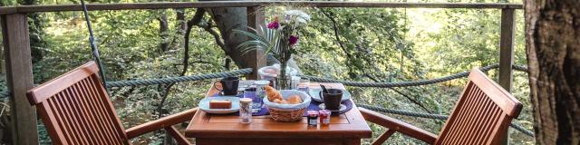 Table avec petit déjeuner sur un balcon d'une cabane dans les arbres en forêt