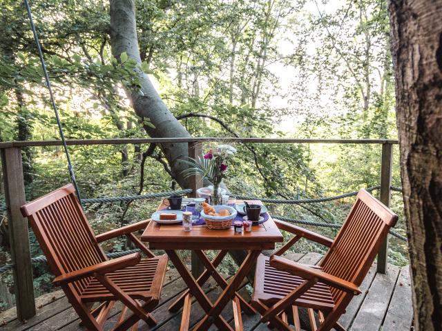 Table avec petit déjeuner sur un balcon d'une cabane dans les arbres en forêt