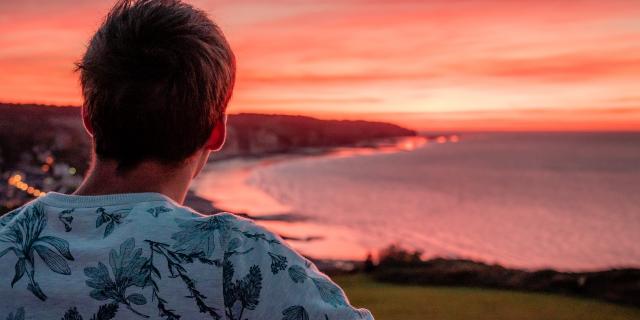 Jeune homme de dos regardant le soleil se coucher sur la plage de Pourville-sur-Mer