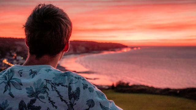 Jeune homme de dos regardant le soleil se coucher sur la plage de Pourville-sur-Mer