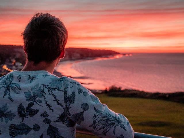 Jeune homme de dos regardant le soleil se coucher sur la plage de Pourville-sur-Mer