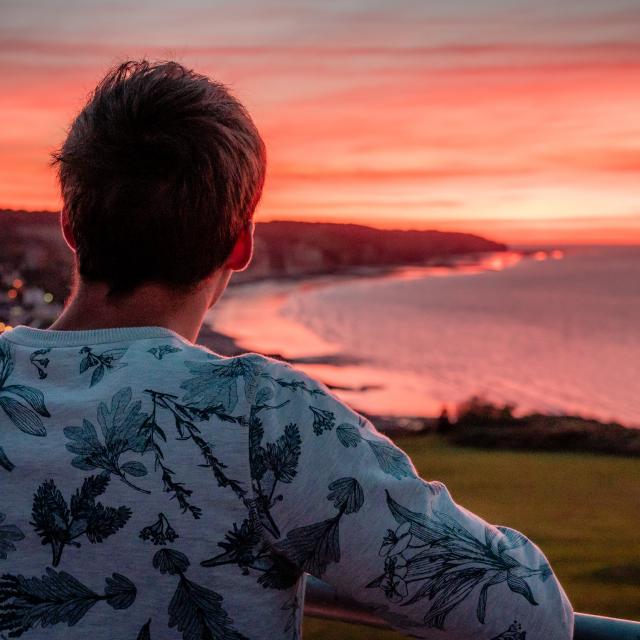 Jeune homme de dos regardant le soleil se coucher sur la plage de Pourville-sur-Mer