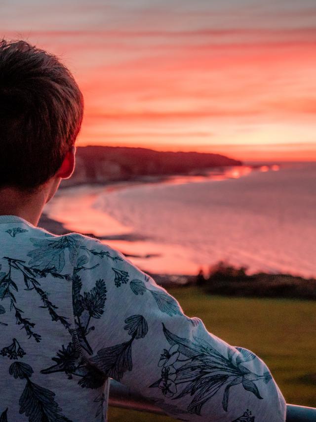 Jeune homme de dos regardant le soleil se coucher sur la plage de Pourville-sur-Mer