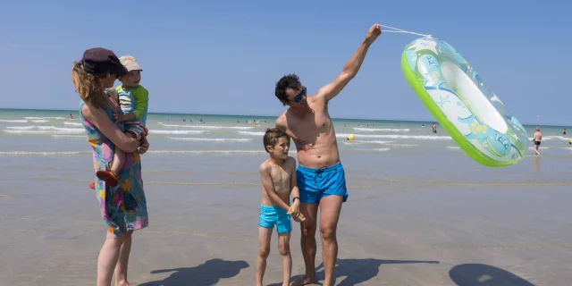 Famille de 4 personnes en maillot de bain sur la plage de Pourville à marée basse. Le papa soulève une bouée.