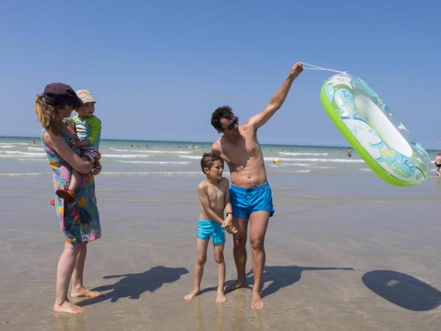 Famille de 4 personnes en maillot de bain sur la plage de Pourville à marée basse. Le papa soulève une bouée.