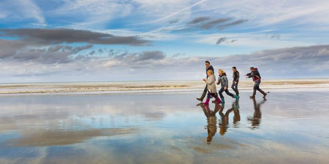 Famille en bottes et tenues hivernales marchant sur la plage à marée basse