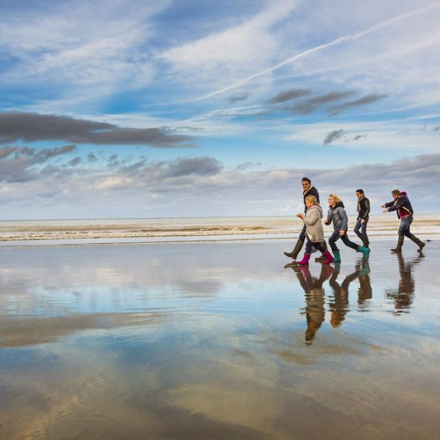 Famille en bottes et tenues hivernales marchant sur la plage à marée basse