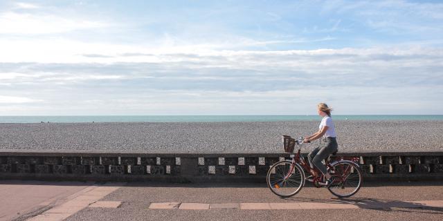 Jeune femme pédalant sur la piste cyclable du front de mer de Dieppe, galets et mer à l'horizon