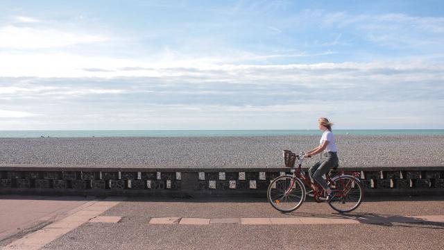 Jeune femme pédalant sur la piste cyclable du front de mer de Dieppe, galets et mer à l'horizon