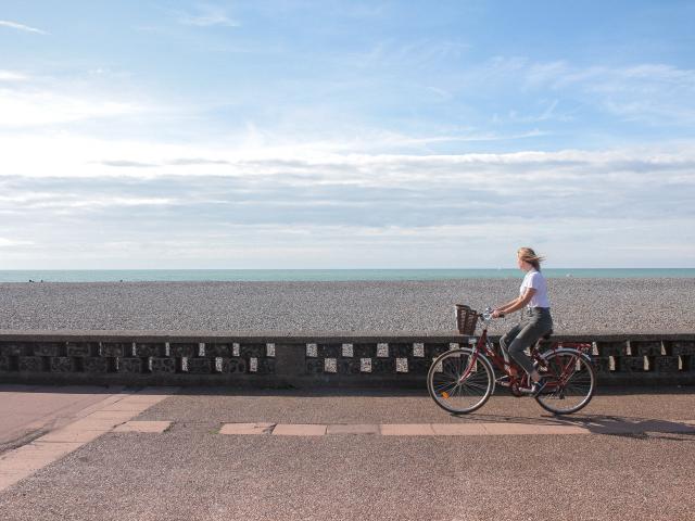 Jeune femme pédalant sur la piste cyclable du front de mer de Dieppe, galets et mer à l'horizon