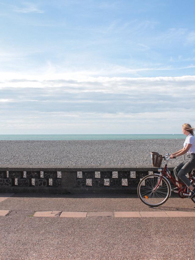 Jeune femme pédalant sur la piste cyclable du front de mer de Dieppe, galets et mer à l'horizon