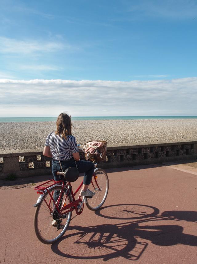 Une jeune femme sur un vélo contemple la plage de Dieppe