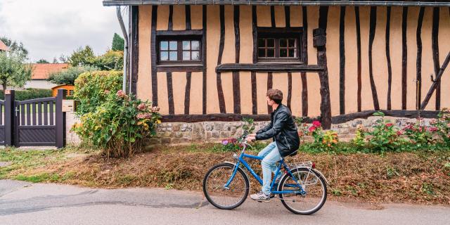 Jeune homme à vélo devant une maison à colombage dans le village de Varengeville-Sur-Mer.