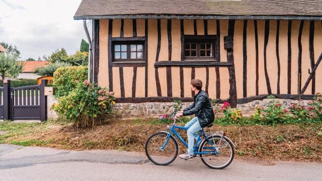 Jeune homme à vélo devant une maison à colombage dans le village de Varengeville-Sur-Mer.