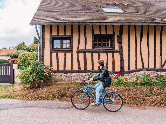 Jeune homme à vélo devant une maison à colombage dans le village de Varengeville-Sur-Mer.