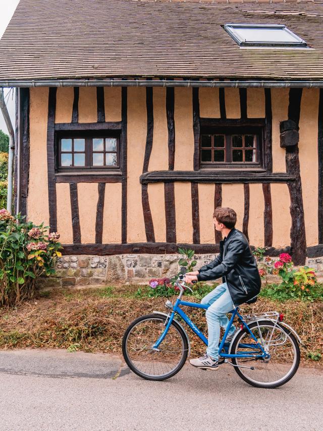 Jeune homme à vélo devant une maison à colombage dans le village de Varengeville-Sur-Mer.