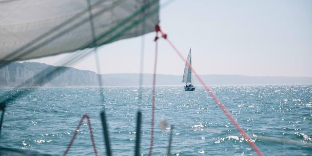 Depuis un voilier, vue sur un autre voilier au large et sur les falaises en arrière plan