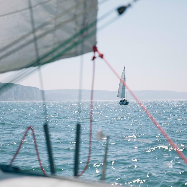 Depuis un voilier, vue sur un autre voilier au large et sur les falaises en arrière plan