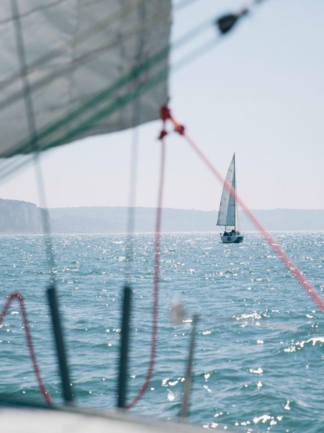 Depuis un voilier, vue sur un autre voilier au large et sur les falaises en arrière plan