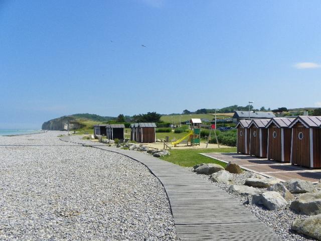 Cabines de plage en bois marron, aire de jeux et planches pour marcher sur les galets. Falaises et mer à l'arrière-plan