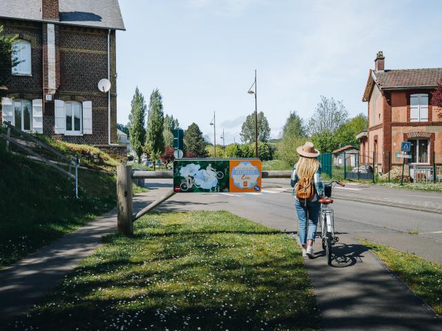 Une jeune femme marche à côté de son vélo sur la fin de la piste cyclable Véloroute du Lin.