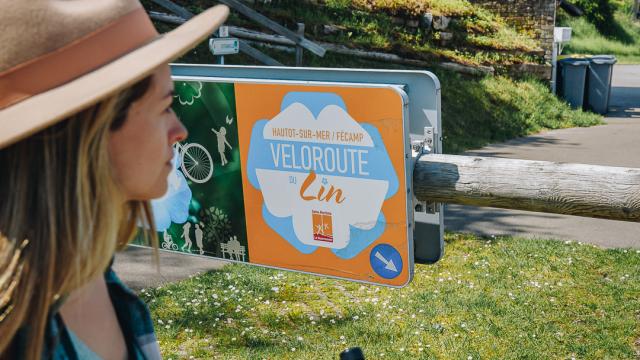 Une jeune femme est devant le panneau du début de la piste cyclable Véloroute du Lin.