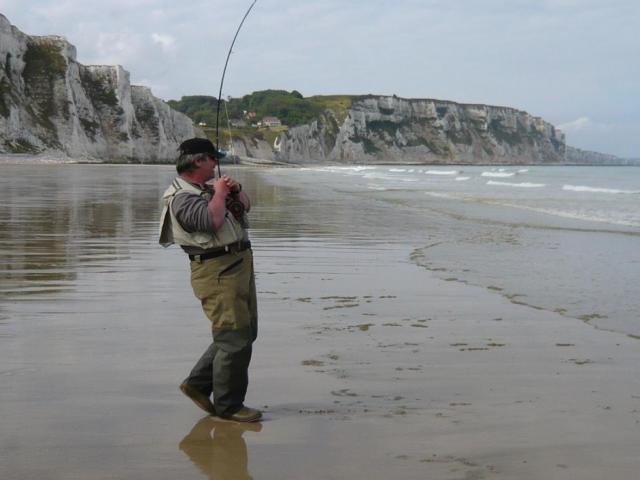 Homme pêchant avec une canne sur la plage, sur le sable. Falaises en arrière-plan.