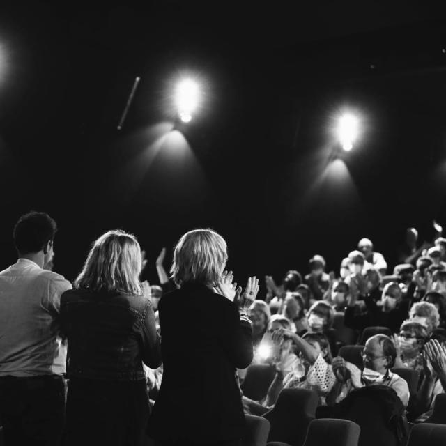 Artistes de dos sur une scène face à un public qui applaudit