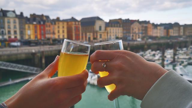 Zoom sur les mains de 2 personnes qui trinquent deux coupes devant le port de plaisance