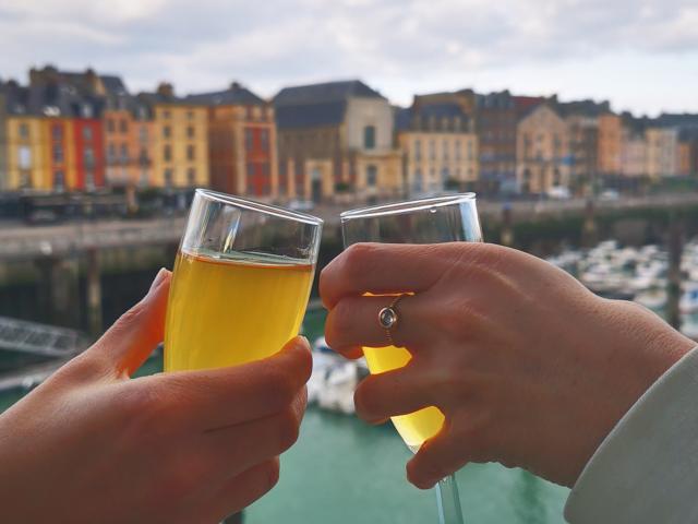 Zoom sur les mains de 2 personnes qui trinquent deux coupes devant le port de plaisance