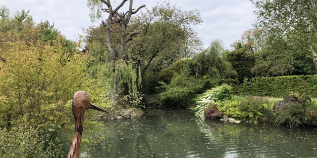 Grande mare entourée de verdure avec une sculpture métallique de cigogne