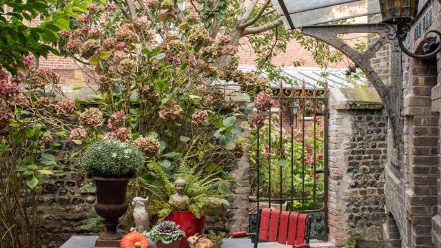 Tables et chaises de jardin sous une marquise dans un petit jardin arboré (arbres, hortensia, fougères)