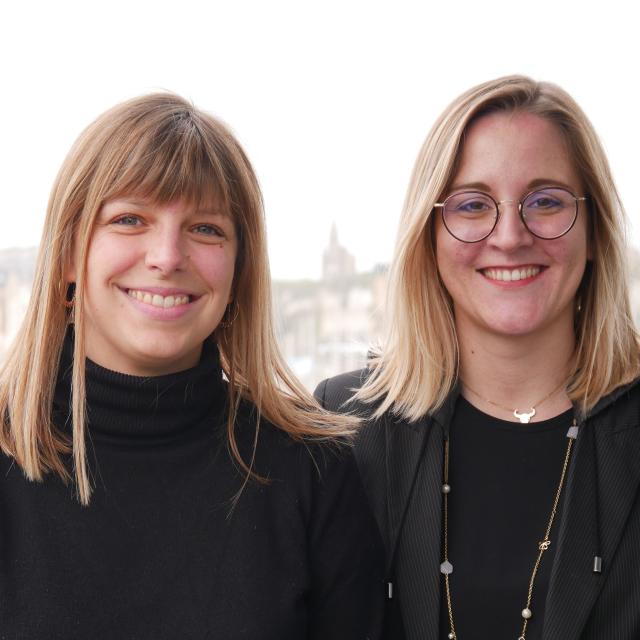 Portrait de 2 jeunes femmes blondes souriantes vêtues de noir devant le port de plaisance