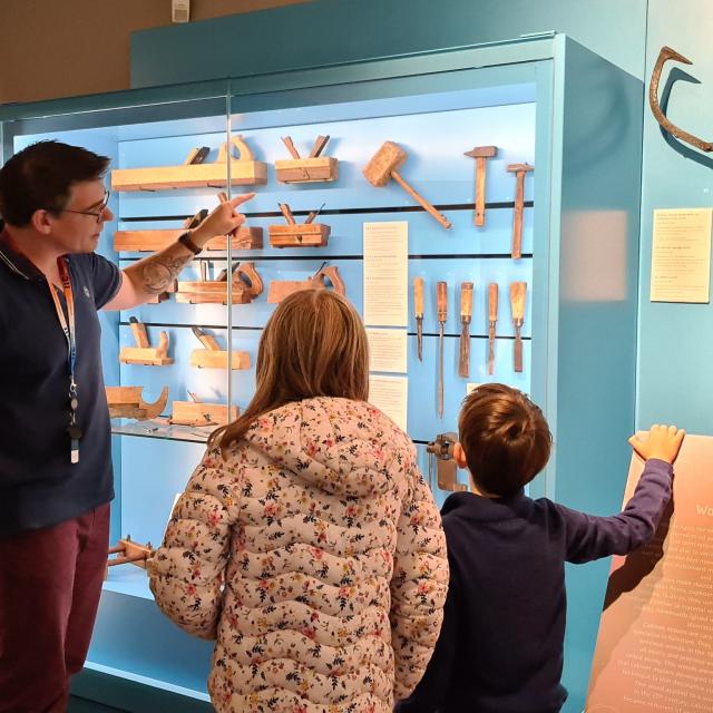 Un guide du musée montre à deux enfant des outils anciens dans une vitrine