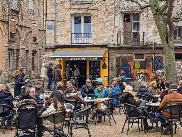 Terrasse pleine de monde d'un bar en centre-ville sur une petite place entourée d'immeubles en briques