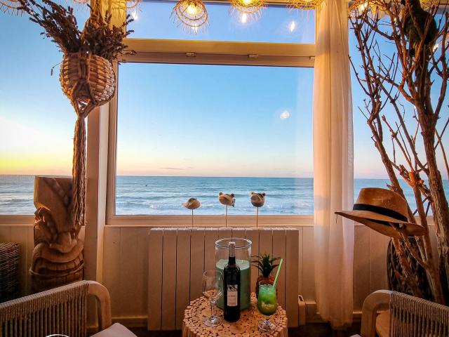 Intérieur d'un bar à l'ambiance chaleureuse et cosy devant une fenêtre vue sur un coucher de soleil au-dessus la mer