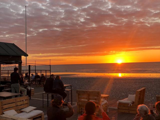 Terrasse d'un bar sur les galets devant un coucher de soleil face à la mer