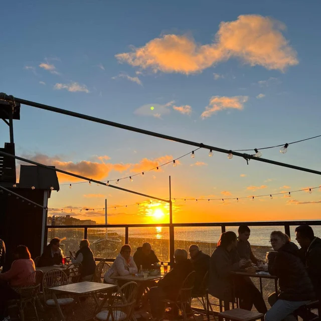 Terrasse d'un bar-restaurant sur les galets devant un coucher de soleil face à la mer