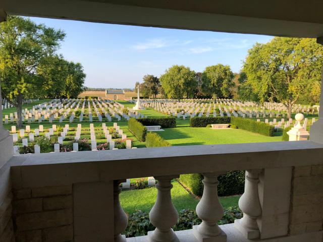 Vue sur un cimetière militaire constitué de centaines de stèles blanches entourées de parterres de fleurs roses et d'arbre verdoyants